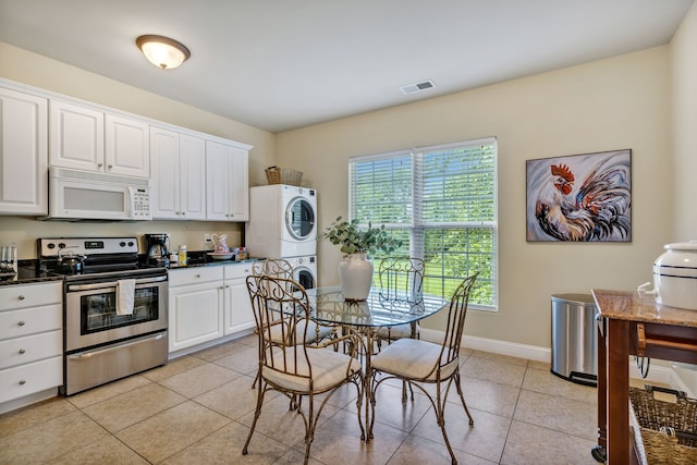 kitchen featuring light tile patterned floors, electric range, stacked washer and dryer, and white cabinets