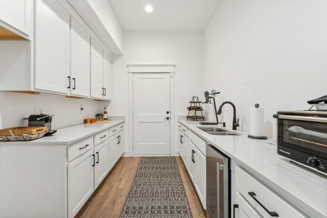 kitchen featuring sink, dishwasher, light hardwood / wood-style floors, and white cabinetry