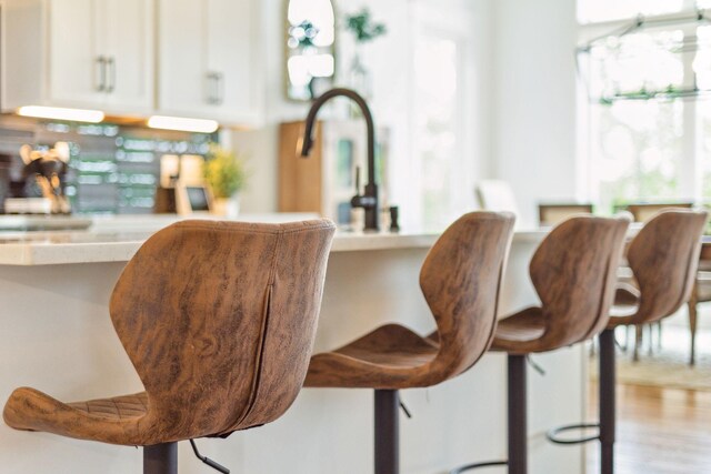 interior details with hardwood / wood-style floors, a kitchen bar, and white cabinets