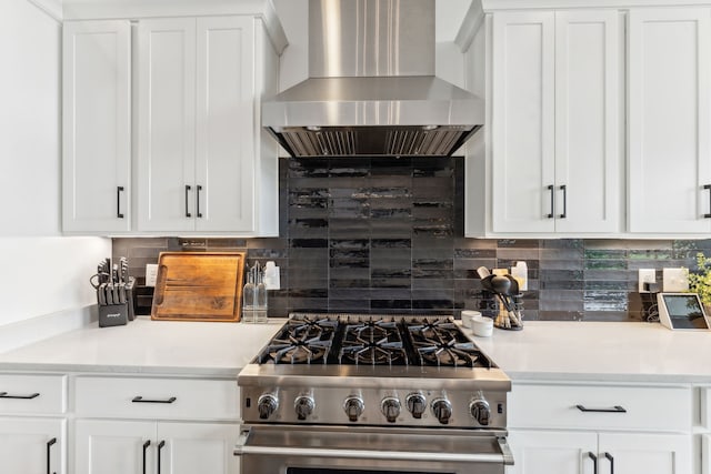 kitchen with wall chimney exhaust hood, high end stove, white cabinetry, and backsplash