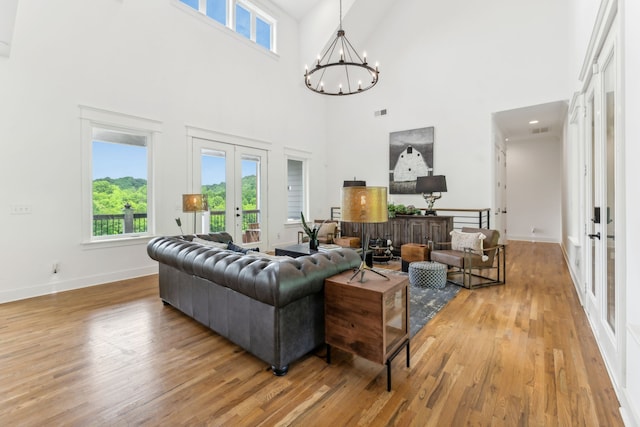 living room with light hardwood / wood-style floors, a towering ceiling, a notable chandelier, and french doors