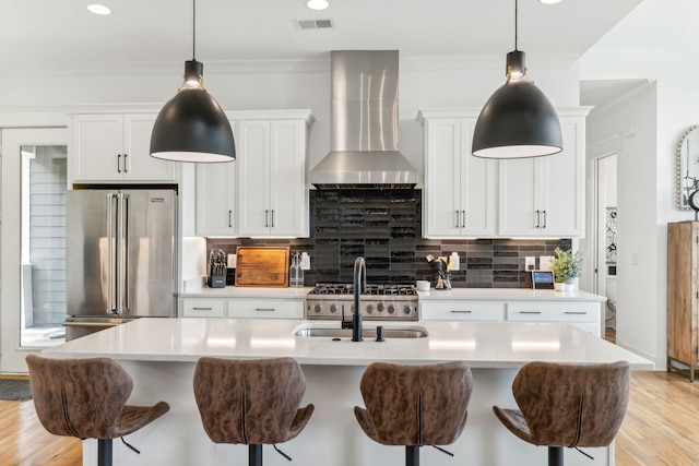 kitchen with high end refrigerator, backsplash, sink, wall chimney exhaust hood, and light hardwood / wood-style floors