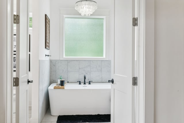 bathroom featuring tile walls, a tub, a healthy amount of sunlight, and a chandelier