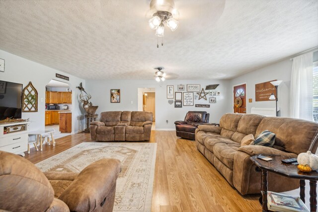 living room with a textured ceiling, ceiling fan, and light wood-type flooring