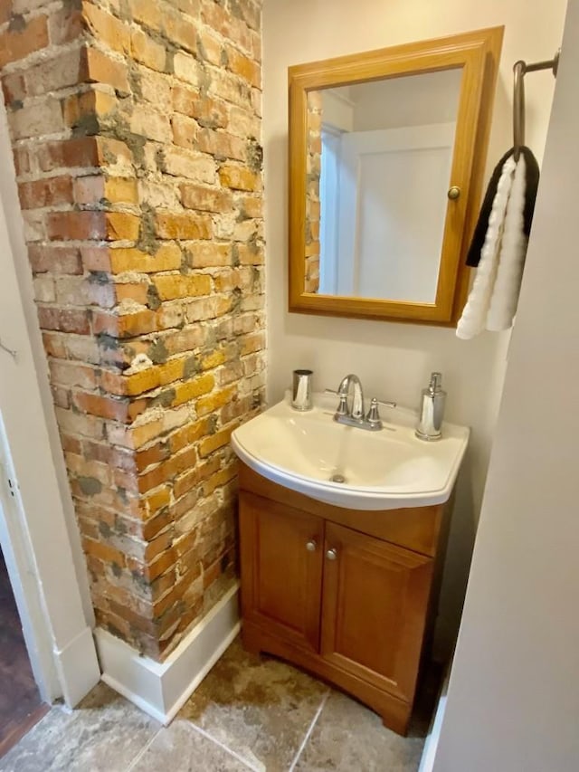 bathroom featuring brick wall, vanity, and baseboards