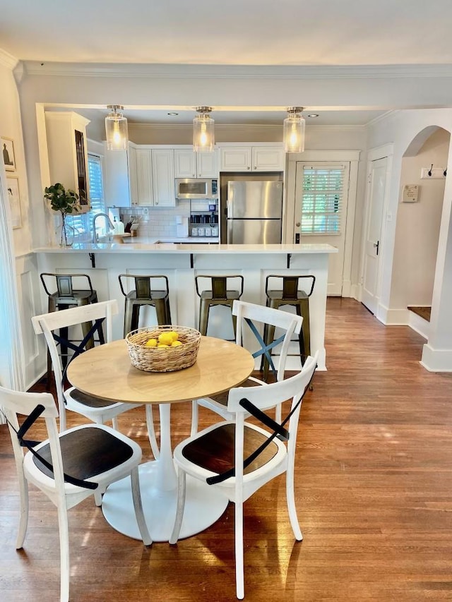 dining area with baseboards, arched walkways, light wood-style floors, and crown molding