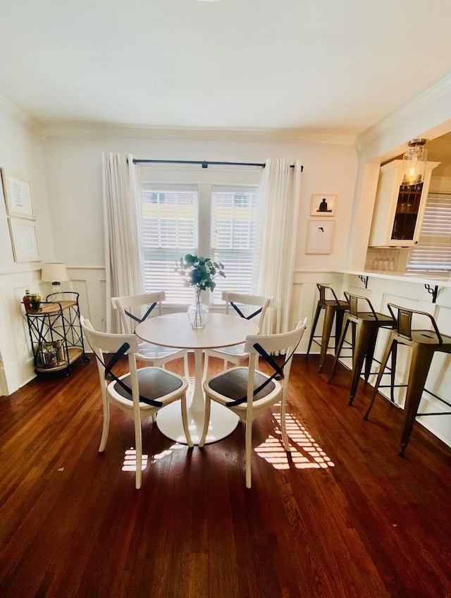 dining area featuring a decorative wall, wood finished floors, wainscoting, and ornamental molding