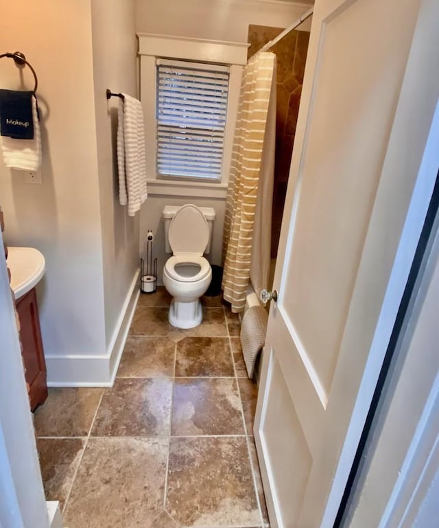 full bath featuring vanity, a shower with shower curtain, baseboards, stone finish floor, and toilet