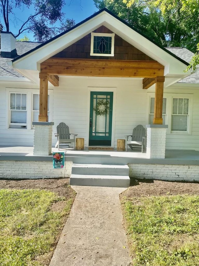 view of exterior entry with a porch and a shingled roof