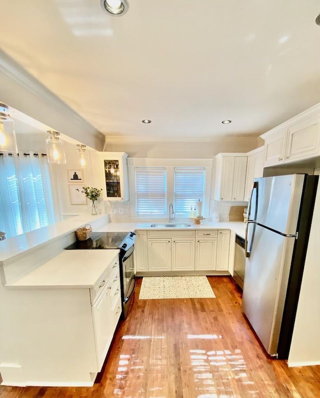 kitchen with light wood finished floors, a peninsula, a sink, light countertops, and appliances with stainless steel finishes