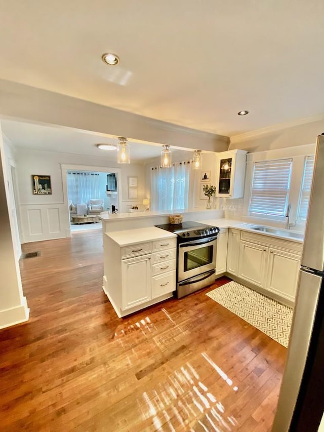 kitchen featuring light wood-type flooring, a sink, freestanding refrigerator, stainless steel range with electric cooktop, and a peninsula