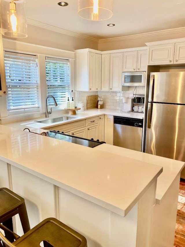 kitchen with backsplash, crown molding, light countertops, appliances with stainless steel finishes, and a sink