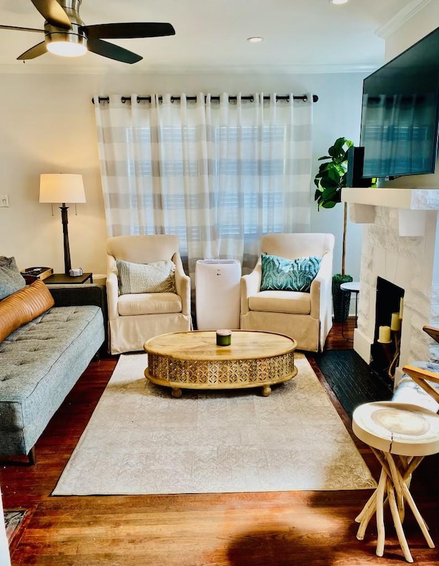 living area featuring a ceiling fan, a premium fireplace, wood finished floors, and ornamental molding