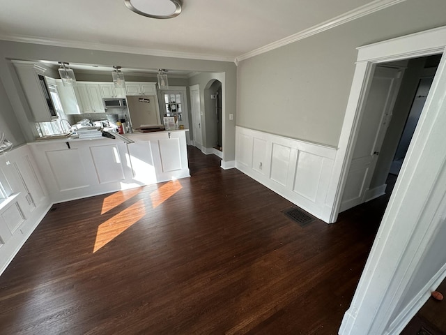 kitchen featuring visible vents, ornamental molding, stainless steel microwave, arched walkways, and a peninsula