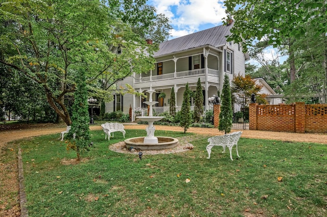 rear view of house with metal roof, a lawn, a balcony, and fence