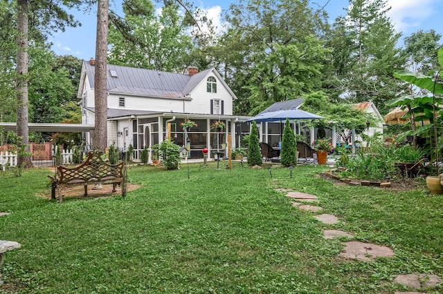 rear view of property with a sunroom, a chimney, metal roof, and a lawn