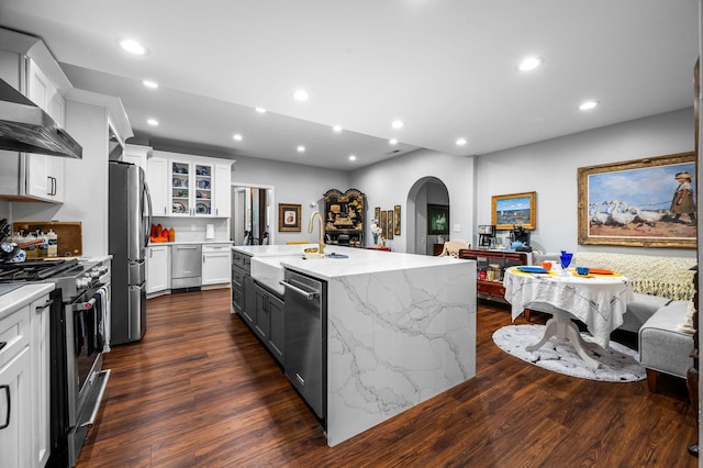 kitchen with arched walkways, stainless steel appliances, recessed lighting, dark wood-type flooring, and wall chimney exhaust hood