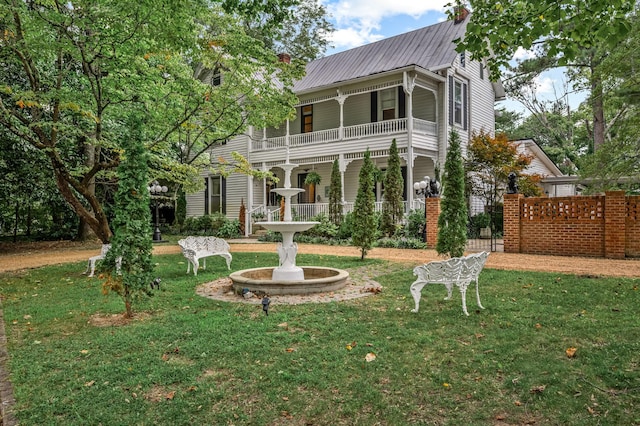 rear view of property featuring metal roof, a lawn, fence, and a balcony