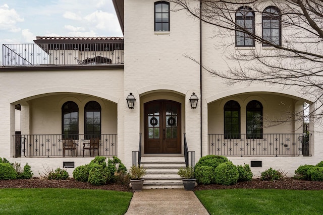 view of exterior entry featuring a porch, a balcony, and stucco siding