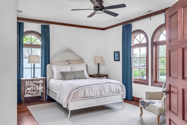 bedroom with ornamental molding, visible vents, ceiling fan, and wood finished floors