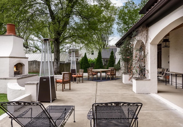 view of patio with outdoor dining space, fence, and a lit fireplace