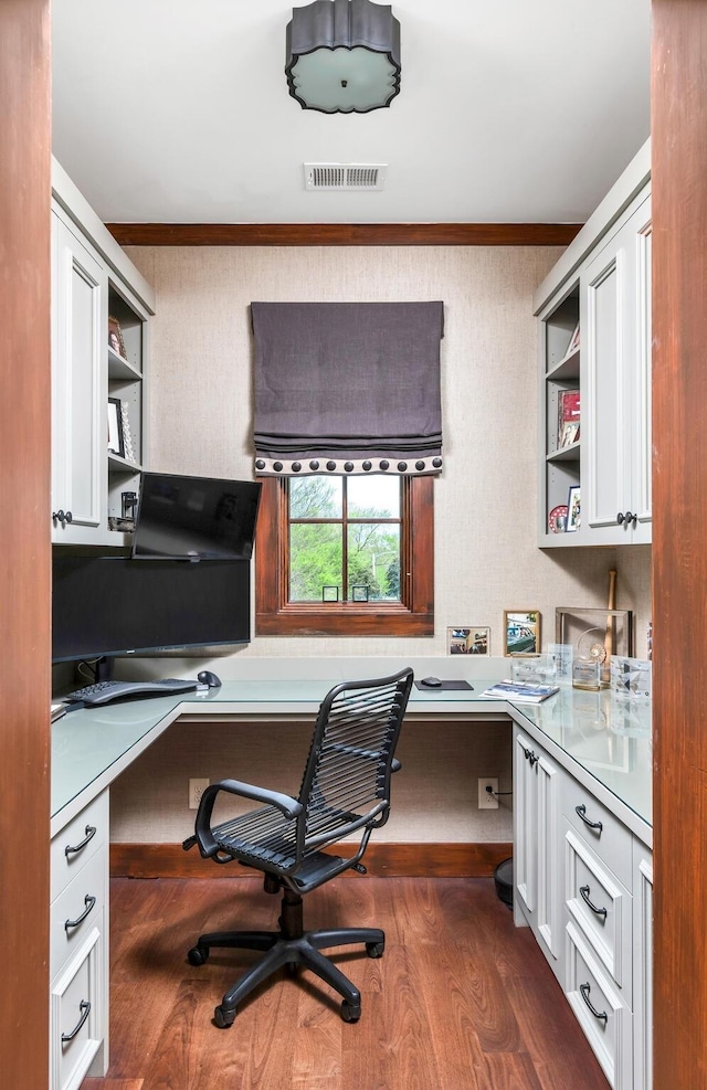 home office with ornamental molding, built in desk, dark wood finished floors, and visible vents