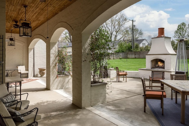 view of patio / terrace featuring a warm lit fireplace and fence