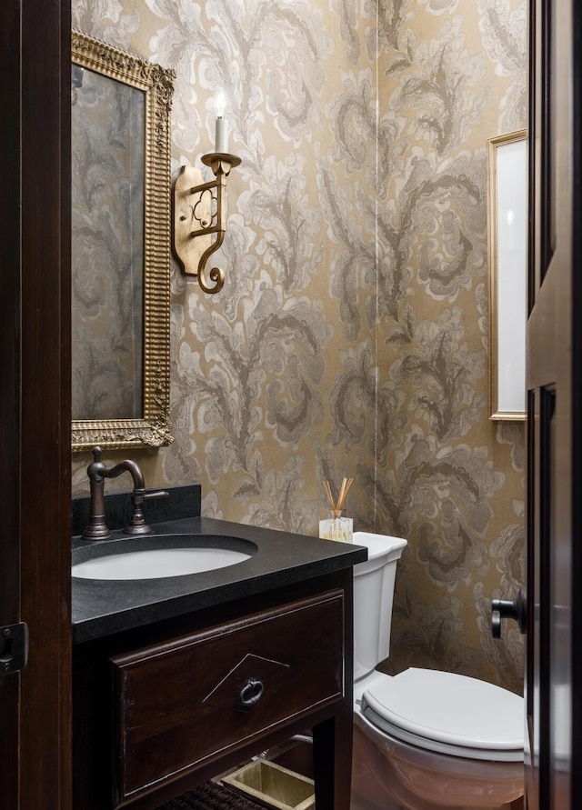 bathroom featuring toilet, wallpapered walls, and vanity