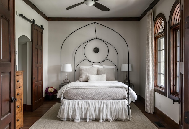 bedroom featuring crown molding, dark wood finished floors, visible vents, a barn door, and baseboards