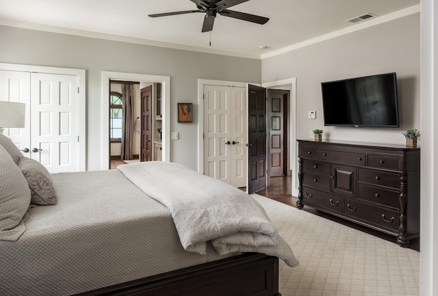 bedroom featuring visible vents, ceiling fan, wood finished floors, crown molding, and two closets