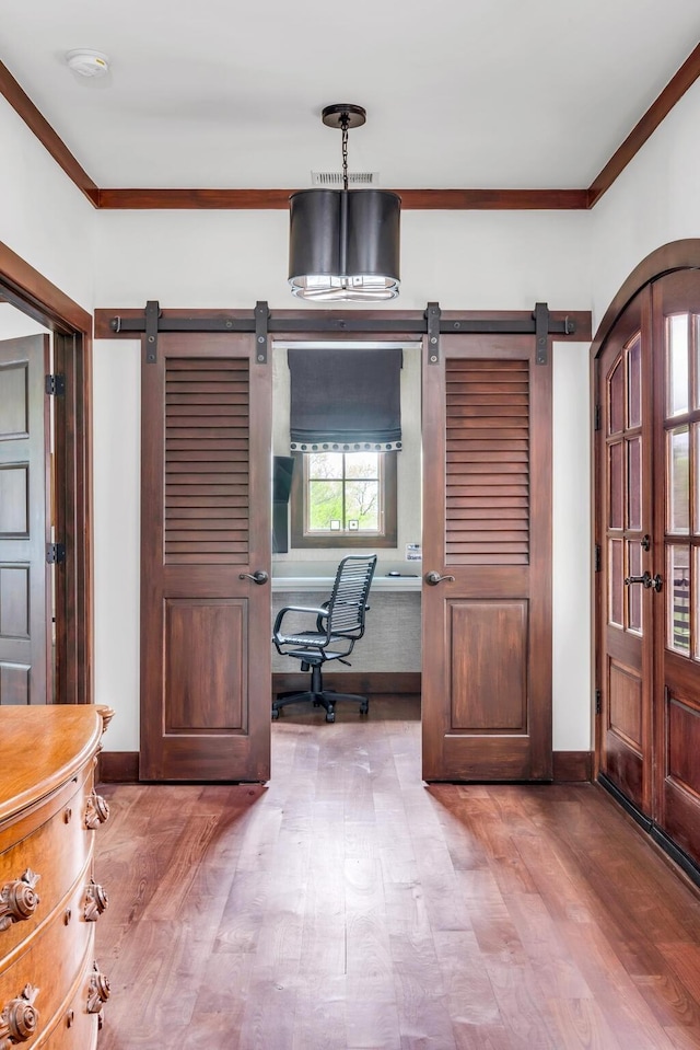 office area featuring arched walkways, a barn door, wood finished floors, baseboards, and ornamental molding