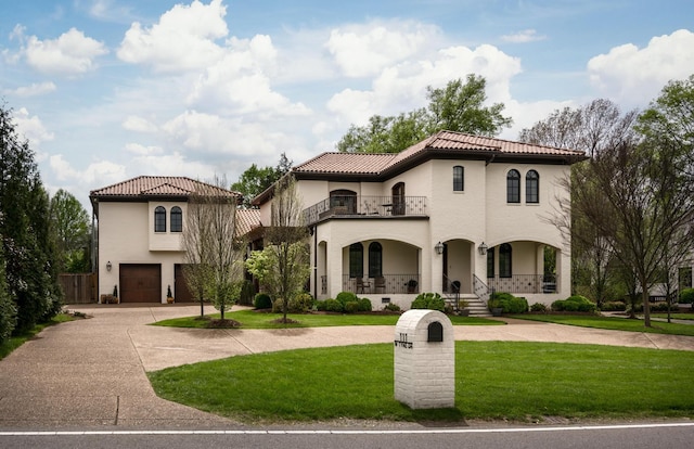 mediterranean / spanish house featuring a tile roof, a porch, a front yard, a balcony, and driveway