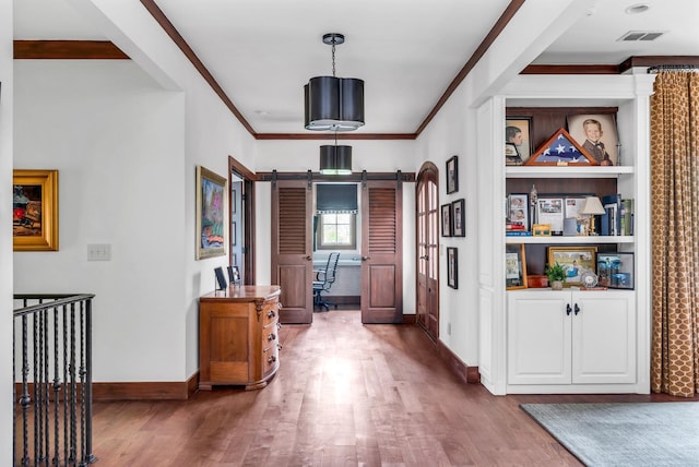 hallway featuring a barn door, baseboards, visible vents, wood finished floors, and crown molding