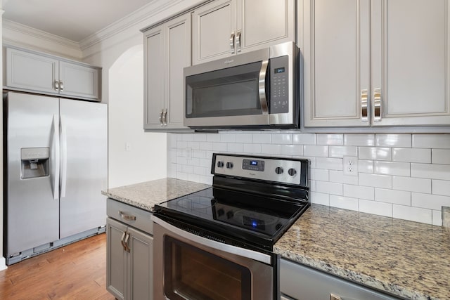 kitchen with backsplash, light wood-type flooring, light stone countertops, gray cabinetry, and stainless steel appliances