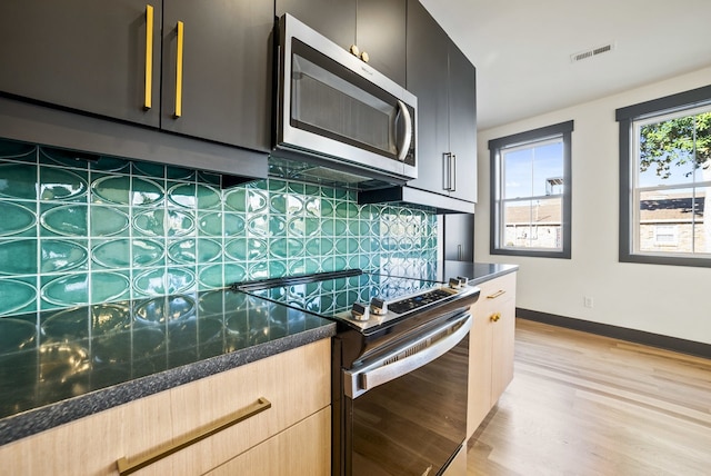 kitchen with backsplash, light hardwood / wood-style flooring, dark stone counters, and stainless steel appliances