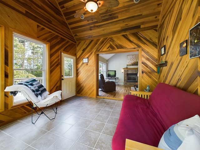 interior space featuring light tile patterned flooring, lofted ceiling with beams, a stone fireplace, and wooden walls