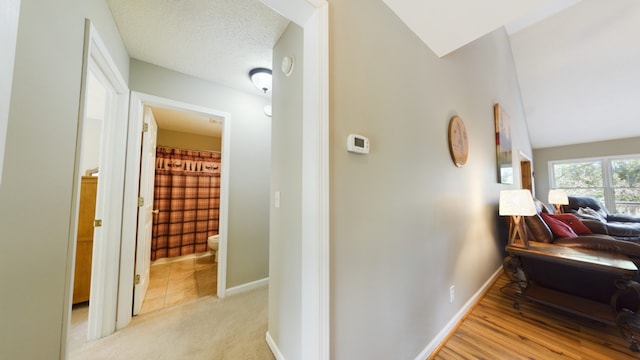 corridor with light colored carpet, a textured ceiling, and lofted ceiling