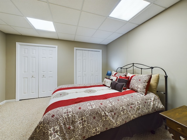 carpeted bedroom featuring multiple closets and a drop ceiling