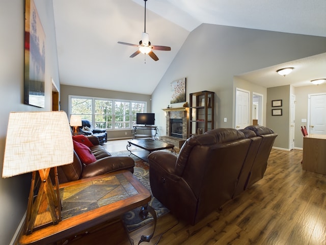 living room with ceiling fan, hardwood / wood-style flooring, a stone fireplace, and high vaulted ceiling