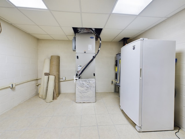 basement with light tile patterned flooring, white refrigerator, electric water heater, and a paneled ceiling