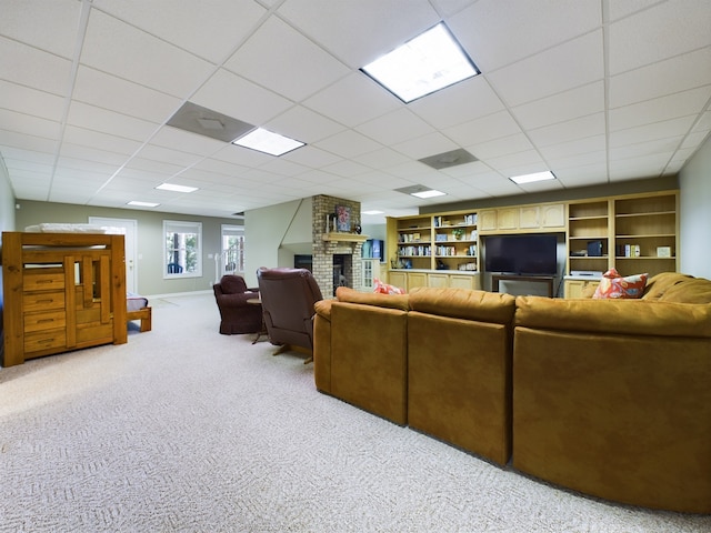 living room with built in features, a drop ceiling, brick wall, light carpet, and a brick fireplace