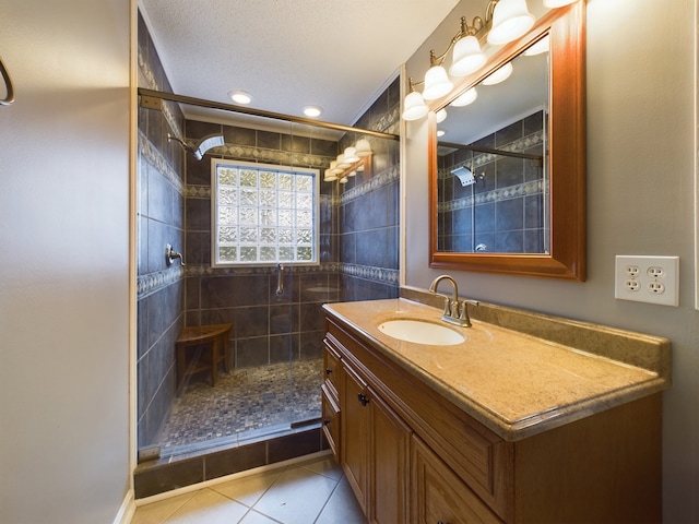 bathroom with tile patterned floors, a tile shower, vanity, and a textured ceiling