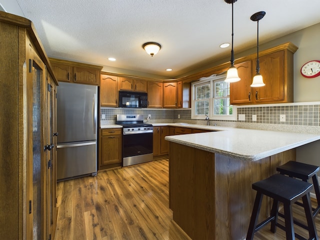 kitchen with stainless steel appliances, dark hardwood / wood-style floors, tasteful backsplash, pendant lighting, and kitchen peninsula