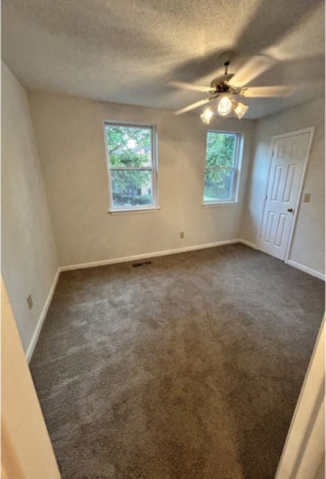 spare room featuring ceiling fan, plenty of natural light, and dark colored carpet