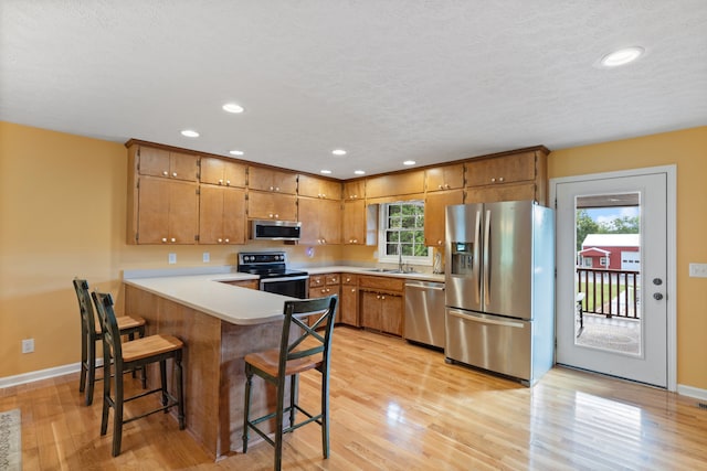 kitchen featuring appliances with stainless steel finishes, a breakfast bar area, light hardwood / wood-style flooring, and a healthy amount of sunlight