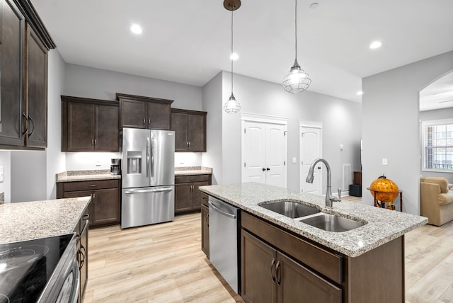 kitchen featuring appliances with stainless steel finishes, light hardwood / wood-style floors, sink, an island with sink, and pendant lighting