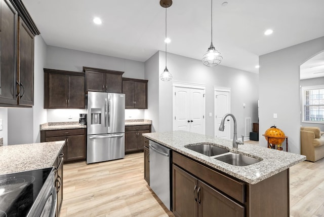 kitchen with arched walkways, appliances with stainless steel finishes, a sink, and light wood-style floors