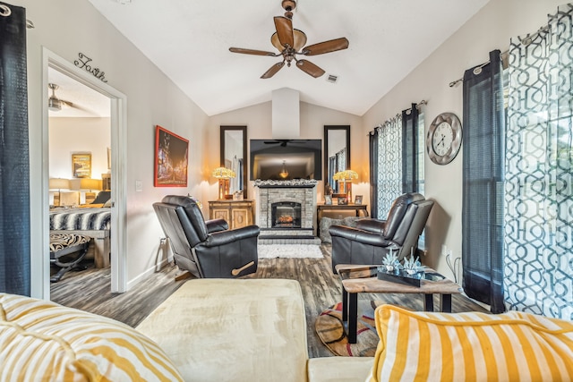 living room featuring ceiling fan, hardwood / wood-style floors, a stone fireplace, and vaulted ceiling