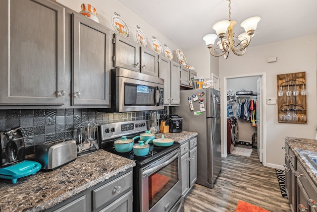 kitchen featuring backsplash, a chandelier, hardwood / wood-style floors, dark stone countertops, and stainless steel appliances