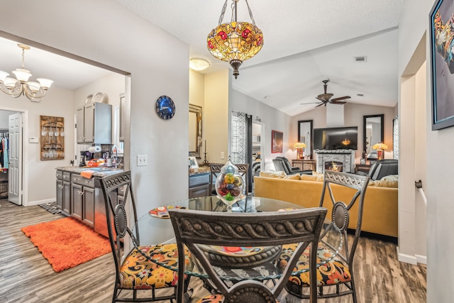 dining space featuring a fireplace, ceiling fan with notable chandelier, vaulted ceiling, and hardwood / wood-style floors